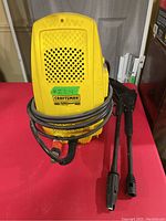 Front view of yellow Craftsman TurboWash 1400 TSS power washer with power cord wrapped and two spray attachments visible
