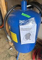 Blue 20 gallon Pressure Abrasive Blaster tank showing user manual attached to the front.