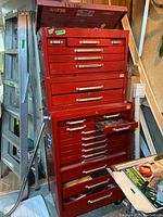 Full front view of the two-piece red metal tool cabinet on wheels, showing top chest with hinged lid open and multiple drawers