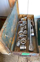 Open metal case showing multiple large sockets and two ratchets with rust and wear inside the case.