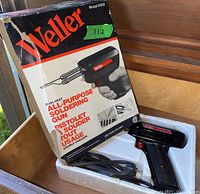 Weller Model 8200 dual heat all-purpose soldering gun in original box with power cord coiled below the gun. Box exterior visible showing product details and model number.
