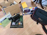 Photo of the Sony video camera with battery and cables, Lowepro camera bag and box, and manuals on a hardwood floor.