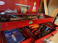 First photo showing the red metal tool chest with open drawers containing various hand tools such as pliers, wrenches, and metal tools.