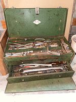 Full view of open green metal tool box showing top compartment with assorted hand tools and bottom drawer containing wrenches and spanners.