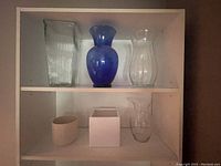 Showing six assorted vases displayed on shelves: three glass vases on top, three smaller vases below.