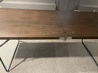 Side view of metal folding table showing wood grain tabletop and metal folding legs.