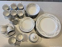 Full set of Somerset by Excel ceramic tableware in white with gray floral and silver rim pattern, showing cups, plates, bowls and cream/sugar containers.