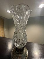 Full view of the crystal vase with silver base on dark surface in a neutral setting, showing the vase's detailed cut pattern and flared top.