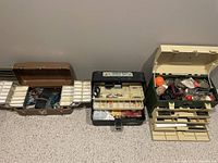 Three vintage fishing tackle boxes opened to show fishing gear inside including lures, hooks, and other fishing accessories.