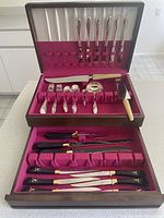 Top view of opened wooden flatware chest showing three sections of flatware including knives, forks, spoons, ladle, carving tools, and cutting utensils with handle details