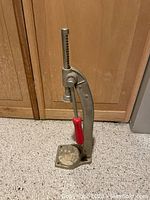 Front view of vintage bottle capper showing red handle, metal frame and base