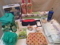 Photo of assorted bath and toiletry items including skincare bottles, cosmetic bags, drawer liners box, pouf, and first aid bag.