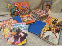 Overview of various British Photoplay magazines and annuals from 1970s and early 1980s displayed on floor, with some stacked and some in blue storage book files.