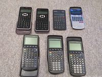 Top view of all seven calculators on carpet showing variety and condition