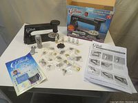 Overview photo showing the main device, multiple accessories, decorative studs in plastic bags, instruction sheet, product box, and a color brochure.