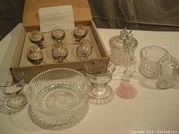 Full view of entire lot showing six sherry glasses, candy dish, scallop shell, and two lidded pots on a surface with cardboard box in background