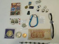 Overview photo showing all items in the lot spread out, including coins, stamps, jewellery, the watch, the banknote, and the small green Tiki figure.