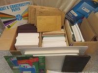 Boxes filled with assorted papers including white bond paper, colored construction paper, and padded manila envelopes