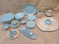 Full set of Poole Pottery Twintone dishes and accent pieces arranged on carpet showing all main components in colors dove grey and sky blue.