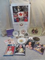 Full view of the lot showing all items including plates, mugs, magazines, the tin tray, and the poster in background.