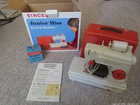Complete lot displayed on floor showing the toy sewing machine, original box, instruction manual, and power adapter box.