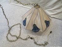 Full view of stained glass light fixture with metal chain and wall plug, showing tapered five-panel design with floral accents.