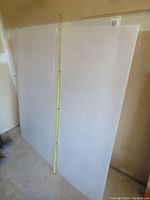 Two white core board sheets standing upright, one showing a vertical measurement tape indicating 4 feet height, with each board having a slit cut halfway down the center.