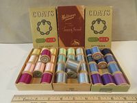 Three open boxes of vintage sewing thread: two Coats Super Sheen boxes with 12 wooden spools each in varied colors, and one box of Beldings Pure Silk thread with 12 light blue/silver wooden spools. Boxes and threads shown with original packaging and labels intact.