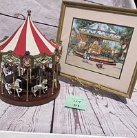 Photo showing the 1990 San Francisco Music Box Company carousel with red and white cloth top and porcelain animals alongside the vintage framed carousel print on decorative stand.