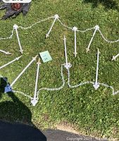 Photo showing white plastic chain-linked fence stakes lying on grass, stakes have skull-shaped connectors, part of the Halloween lawn decoration set.