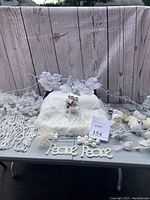 Photo showing a variety of white Christmas ornaments, two different white bead garlands, a fluffy white tree skirt with reindeer, and 'Peace' decorations arranged on a table with a wood plank backdrop.