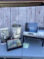 Full view of Marinade Master vacuum marinade machine showing clear drum and digital controls, and Juiceman II juicer with waste container and accessories including a cookbook.