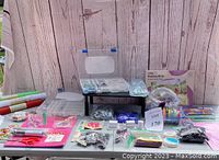 Wide view of all crafting supplies on the table, showing beads, scissors, thread, ribbons, felt rolls, boxes, and bags of accessories.