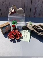 Wide view of fish tank accessories on table showing resin coral, driftwood, plastic container, Florida magnet, small palm tree and box