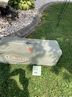 Graco storage carry bag with zipper and logo on green fabric, bag placed on grass with lot sign.