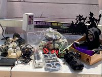 Overview photo showing all Halloween decorations including string lights, monster figurines in plastic bag, ice cube trays, caution tape, blacklight packaging, skeletal figure, and cat silhouette decoration