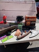 Photo showing entire lot including cauldron, fake hand, blood bottle, axe, knife, pipe, bone, signage, luminaria kit, and blood-stained cloth.