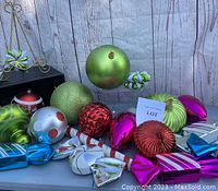 Multiple large colorful plastic Christmas ornaments in various shapes and finishes arranged on a white table against a wood backdrop.