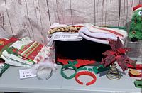 Display of various Christmas tablecloths, placemats, napkins, and red and green themed holiday headbands including reindeer antler and Santa hat designs.