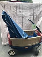 Side view of the Little Tikes Deluxe Ride and Relax Wagon showing beige and red panels, blue base and partially folded blue umbrella canopy.