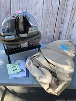 Photo showing Bissell SpotBot cleaner with power cord, flexible hose, along with folded beige patio heater cover and instruction manuals on table