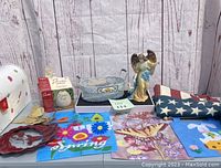 Overview of all items on the table including mailbox, Patio Egg warmer, flags, tin bin, angel figurine, and hummingbird wind spinner.