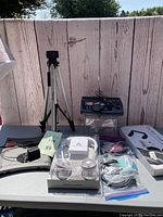 Full view of lot items on table including tripod, neck fan, boxed auto headrest, scanner, HDMI cables and accessories