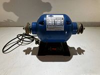 Front view of blue 3/4 HP bench grinder showing label with specifications and power switch on black base.