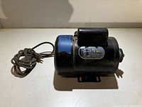 Side view of black electric motor showing motor body, capacitor and power cord coiled beside it.