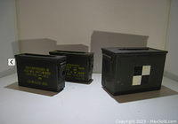 Photo of three military style ammo cans on a light surface showing front and side views with labels and markings.