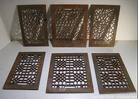 Photo displaying six antique metal vent covers arranged in two rows on a flat white surface. Each vent cover has a rusted patina with distinct intricate geometric cutout designs.