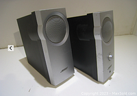 Two Bose computer speakers from a side angle, showing one with volume knob and some wear on silver front panel.