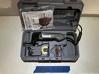 Dremel multi tool and accessories organized in molded plastic case, showing included sanding pads, cutting wheels, and user manual.