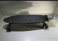 Top and side view of black E-rasm electric skateboard with battery pack wrapped in plastic at rear.